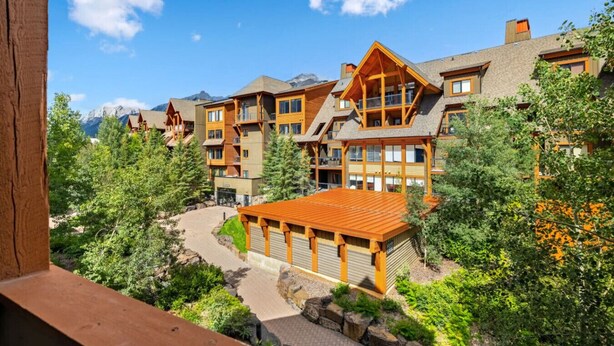 Eine mehrstöckige Lodge mit einer zentralen Holzkonstruktion, umgeben von Bäumen und Bergen im Hintergrund.
