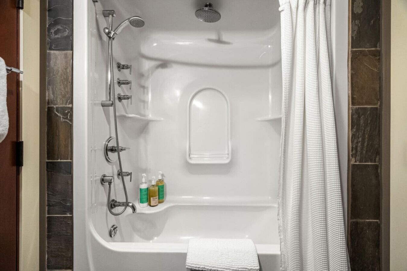 A bathroom with a bathtub, shower, and two shelves with toiletries.