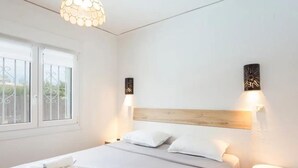 Une chambre d’hôtel avec un grand lit, deux tables de chevet, une fenêtre avec des stores blancs et un luminaire au plafond.