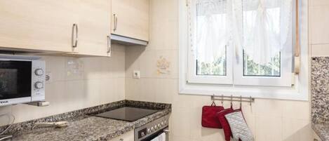 Cuina amb microones, forn, taulell de granat i finestra amb cortines.