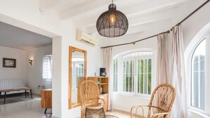 Une pièce spacieuse avec une grande fenêtre, une table ronde entourée de chaises, une bibliothèque et un miroir au mur.