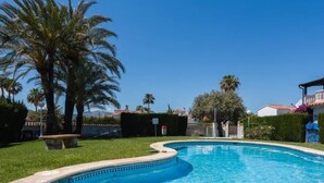 Une piscine à bord incurvé, entourée d’une pelouse bien entretenue et de palmiers.