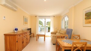 A spacious living area with a wooden cabinet, a television, a sofa, and a dining table with chairs. - 3-bed apartment, sea view - 6 guests (Denia)