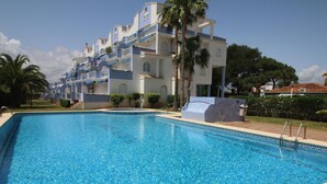 A swimming pool with clear blue water, surrounded by a building with multiple balconies and palm trees. - 3-bed apartment, sea view - 6 guests (Denia)