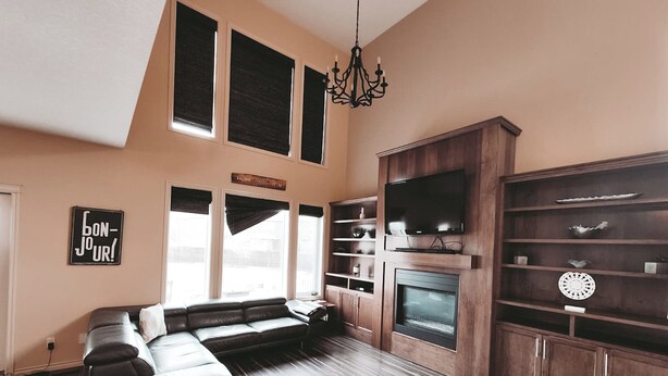 A living room with a sectional sofa, a fireplace, wooden shelving, and a chandelier. - Lake Community Retreat - Family Parks (Calgary)
