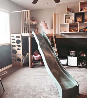 A room with a slide, a playpen, and a fireplace.