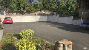 Uma área de estacionamento com um carro vermelho, cercada por vegetação e árvores.
