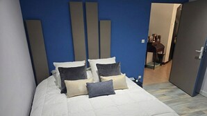 Cama bem arrumada com edredom branco e várias almofadas em quarto com paredes azuis e piso de madeira.