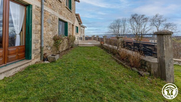 Ein Gebäude aus Stein mit grünen Fensterläden, einem grünen Hof und Blick auf das Meer.
