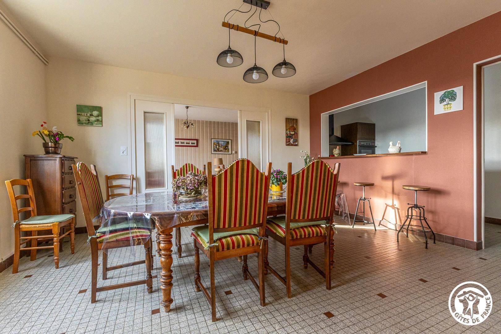 Un comedor con una mesa y sillas de madera, una cocina al fondo y un suelo de baldosas.