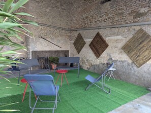 A rustic outdoor seating area with stone walls, a fire pit, and artificial grass.