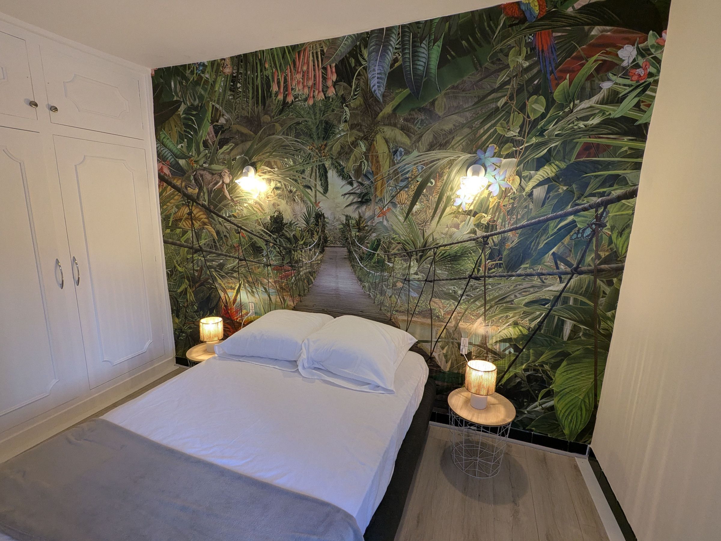 A bedroom with a bed, two bedside lamps, and a mural of a jungle scene.