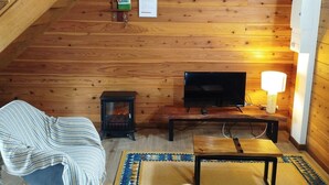 A cozy cabin interior with a wooden ceiling, a fireplace, a television, and a comfortable seating area.