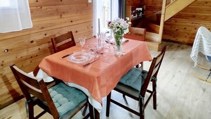 A wooden cabin with a dining table set for four, featuring a peach-colored tablecloth, clear glassware, and a vase with flowers.
