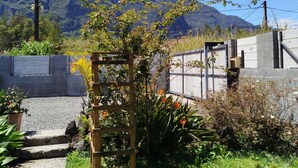 A garden with a wooden trellis, a concrete wall, and a mountain in the background.