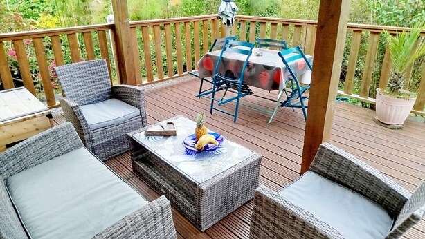 A covered outdoor patio with wicker furniture, a table with a tablecloth, and a potted plant.