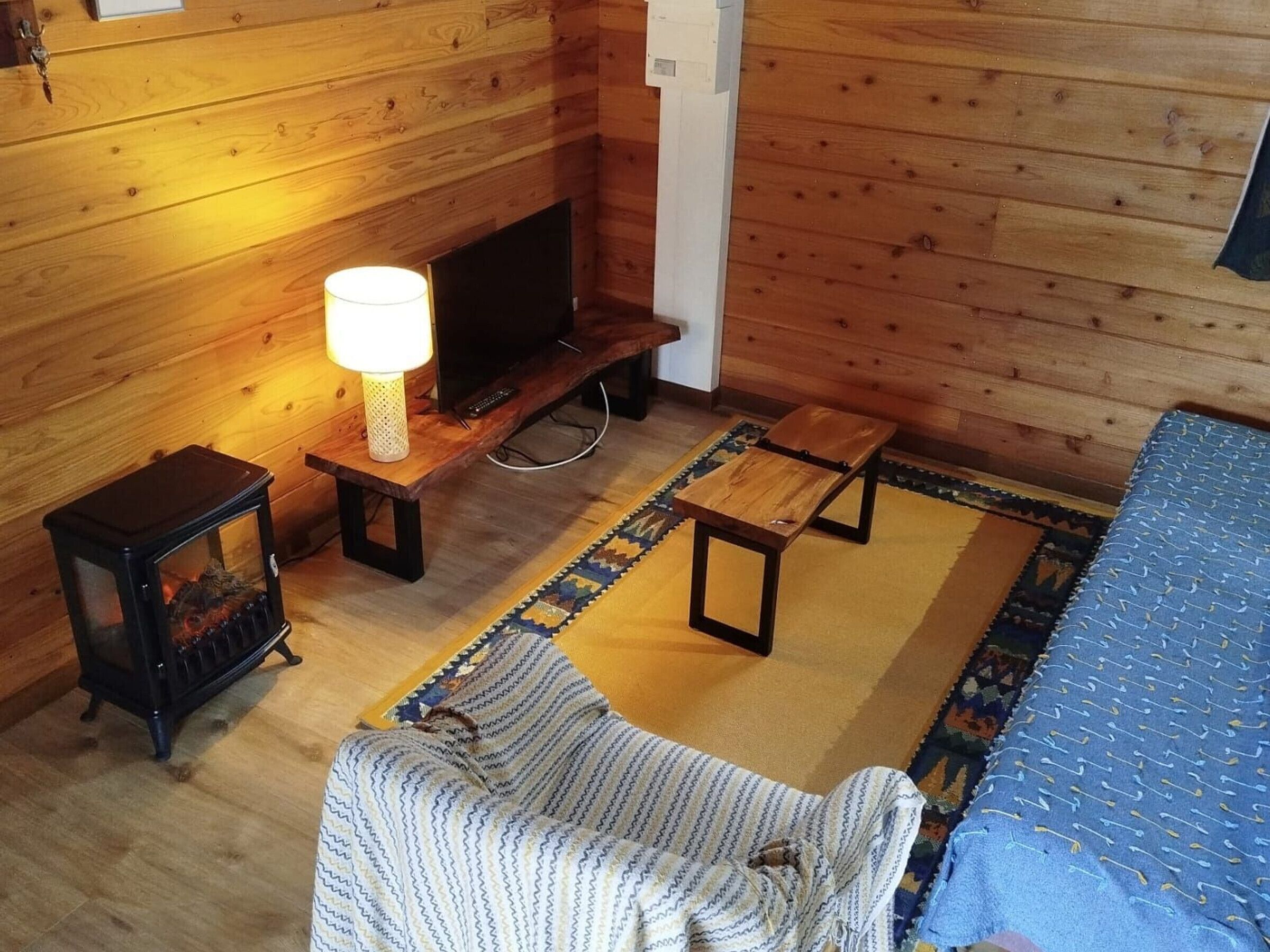 L’intérieur d’un chalet accueillant, avec un plancher en bois, un canapé, une petite table avec une lampe, un téléviseur et un tapis à motifs.
