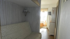 Una habitación con un sofá estampado, un estante con objetos y una puerta que da a una zona de cocina.