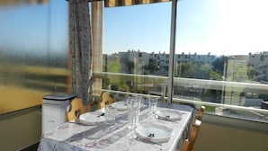 Comedor con una mesa dispuesta para cuatro, ventanas amplias con vistas a la ciudad y una lámpara de techo.
