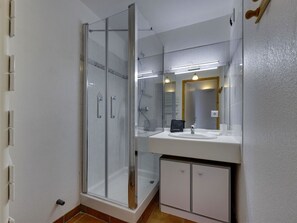 Ein modernes Badezimmer mit einer gläsernen Duschkabine, einem weißen Waschbecken und einem Spiegel darüber.