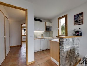 A compact kitchen with white cabinets, a stone accent wall, a microwave, and a sink. - Charming apartment, mountain view - 4 guests (Montvalezan-La Rosière)