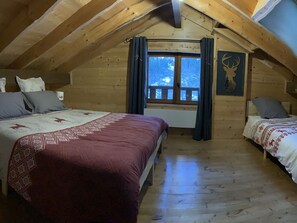 A cozy attic bedroom with two beds, wooden beams, a window with curtains, and a deer wall art. - Spacious chalet - 10 guests (Châtel)