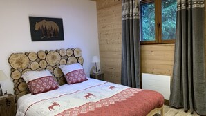 Una camera da letto con un letto, una testiera in legno, un comodino, una lampada, una finestra con tende e un quadro appeso al muro.