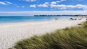 Une plage de sable blanc, un ciel bleu azur et une côte lointaine parsemée de bâtiments.