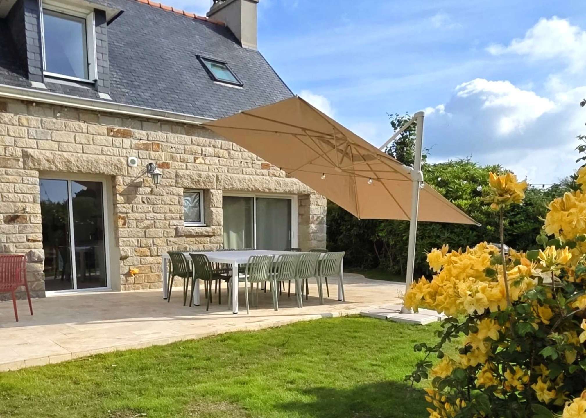 A stone house with a patio, a table with chairs, and yellow flowers.