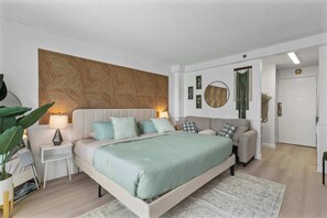 A modern bedroom with a large bed, bedside tables, a sofa, and a decorative headboard. - Memory Foam King Bed • Snorkels • Walk to Beach (Honolulu)