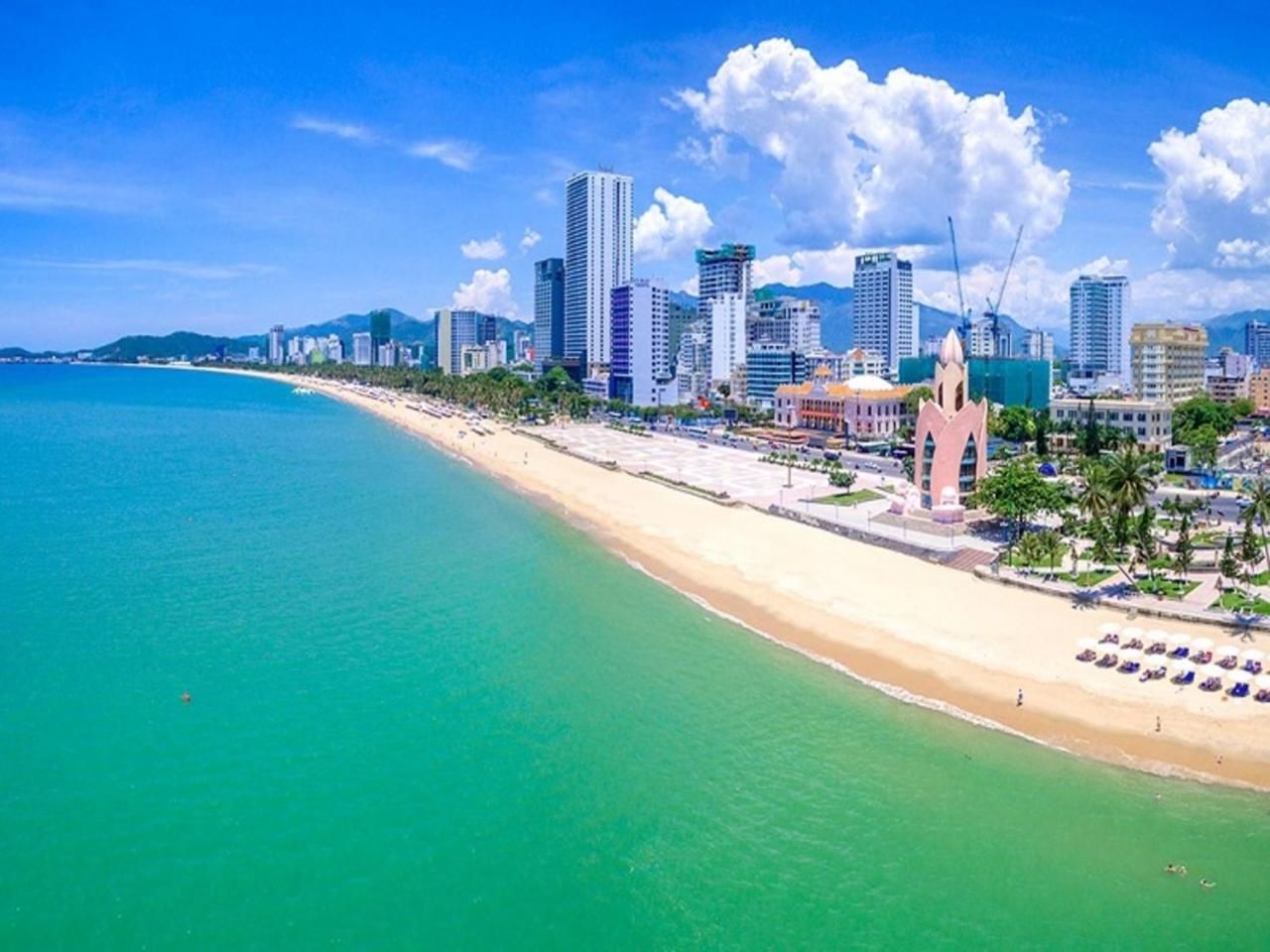 Un paysage urbain côtier avec une plage, des immeubles de grande hauteur et un bâtiment rose remarquable surmonté d’un dôme.