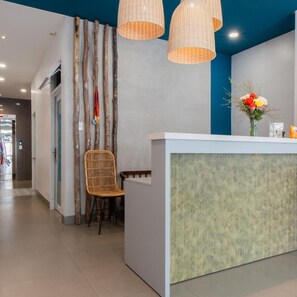 A reception area with a white counter, a wicker chair, and a wall with vertical lines. - Shoho Hotel Nha Trang (Nha Trang)
