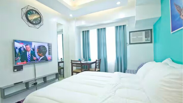 Habitación de hotel con una cama grande, un escritorio, una silla, un televisor y una ventana con cortinas.