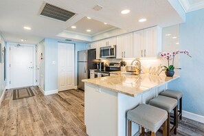 A modern kitchen with white cabinets, stainless steel appliances, and a marble countertop. - 🐠 HIGHLY RATED! Remodeled Sea Winds Beachfront 10th Floor Double Vanity Sinks (Marco Island)