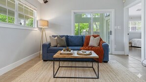 A living room with a blue sofa, a coffee table, a floor lamp, and a view through a glass door. - Authentic Central Austin Family Retreat | Southern Charm Near Downtown ❤️ (Austin)