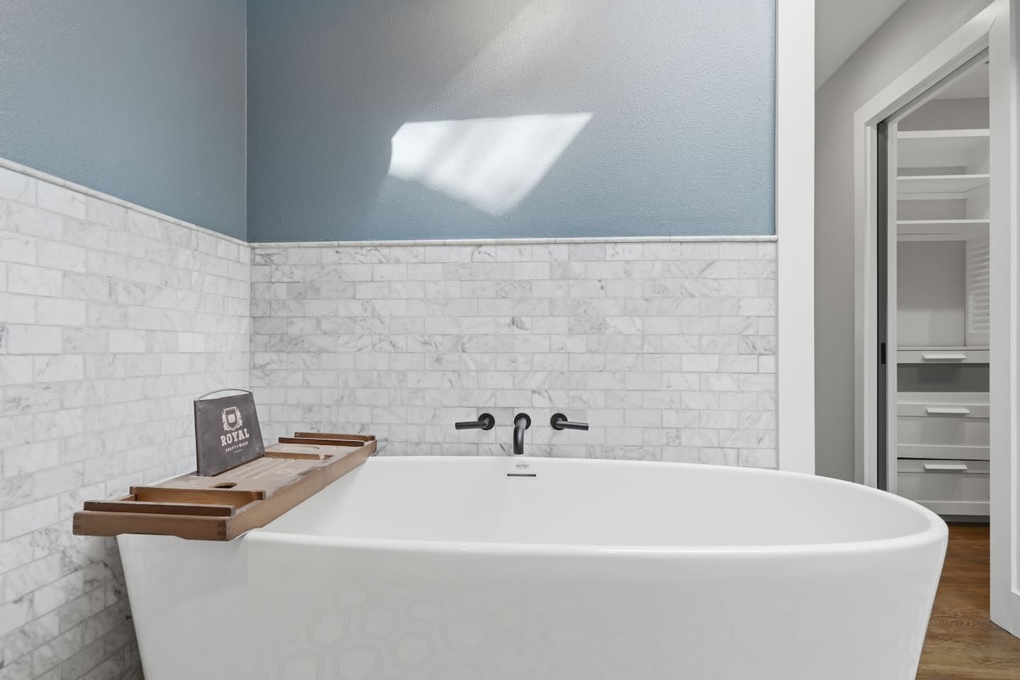 Ein modernes Badezimmer mit einer freistehenden Badewanne, einem Holztablett mit einem Handtuch und einem Handtuchhalter.