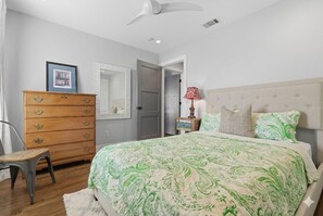 A bedroom with a bed, dresser, chair, and a ceiling fan.