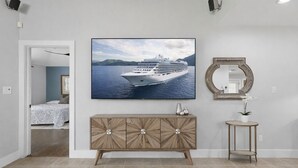 A room with a large framed picture of a cruise ship, a wooden cabinet, a round mirror, and a small table with a potted plant. - Authentic Central Austin Family Retreat | Southern Charm Near Downtown ❤️ (Austin)