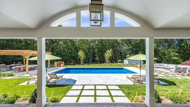 Ein überdachter Außenbereich mit Pool, Terrassenmöbeln und einer Pergola.