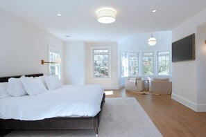 A bedroom with a large bed, a desk, and a chair, with windows and a ceiling light. - Brand New Osterville
Luxury Estate Sleeps 18 (Barnstable)