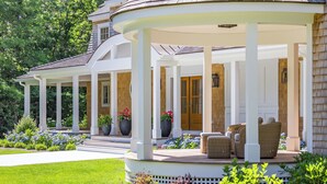 Eine überdachte Veranda mit Säulen, Gartenmöbeln und einem gepflegten Garten.