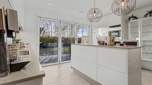 Eine moderne Küche mit einer großen Kochinsel, Schiebetüren zu einer Terrasse und Pendelleuchten.