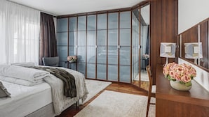 Ein Schlafzimmer mit einem Bett, einem Sessel, einem Schreibtisch mit Blumen und einem Schiebeglastüren-Kleiderschrank.