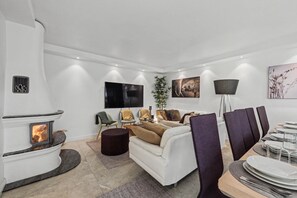 A modern living room with a white fireplace, a sofa, a dining area with chairs and a table set for four, and artwork on the walls.