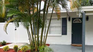 A residential building with a white exterior, a dark blue door, and a small garden area with red mulch and various plants. - Peacefull & Central 2-bedroom house with AC in sunny Tampa (Tampa)