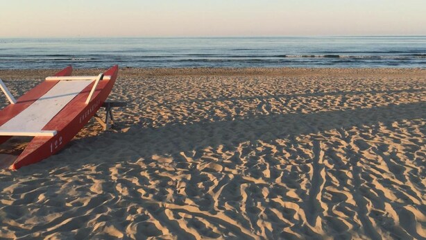 A beach with a red lounge chair and a white towel. - Hotel Latini (Rimini)