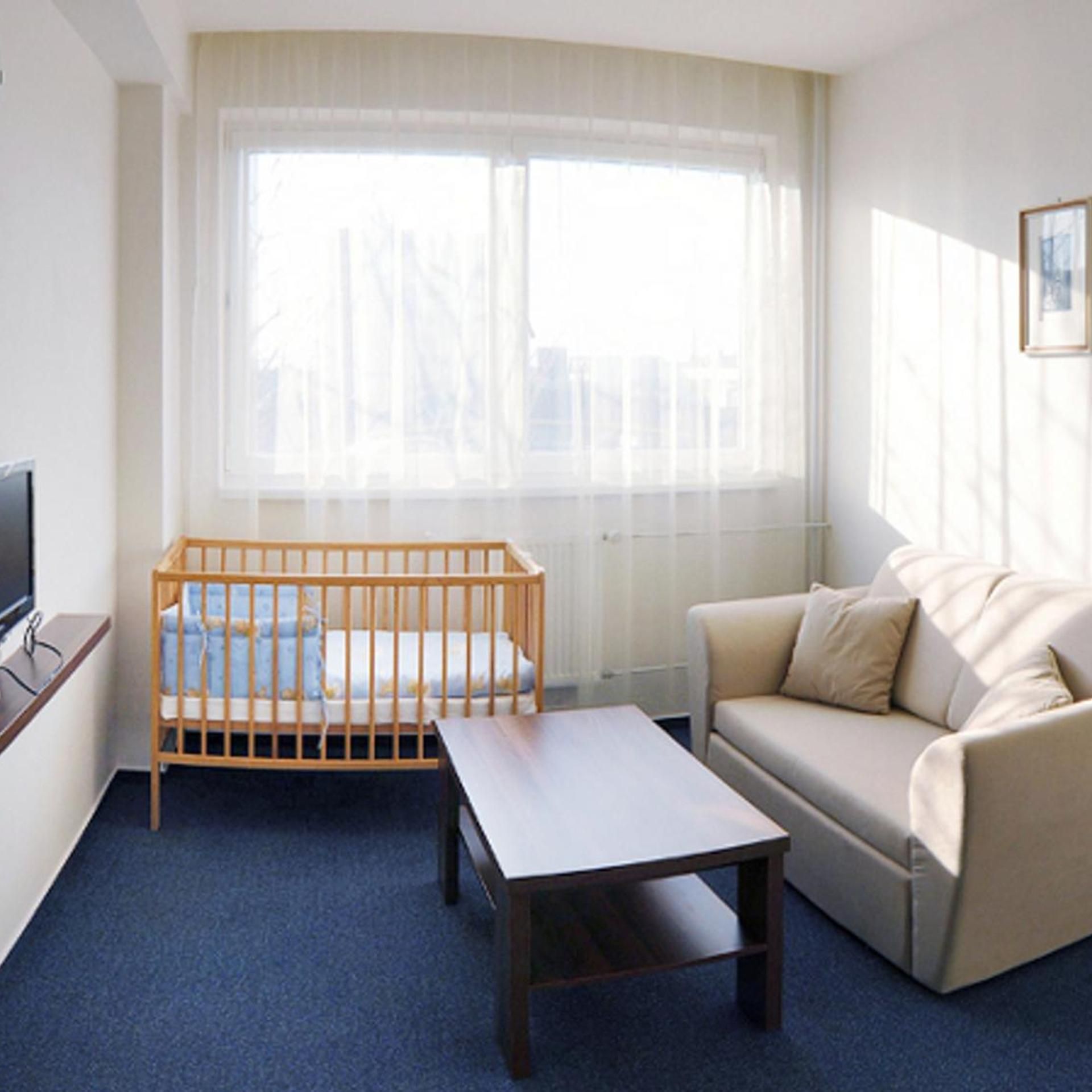 A hotel room with a crib, a sofa, a coffee table, and a television.