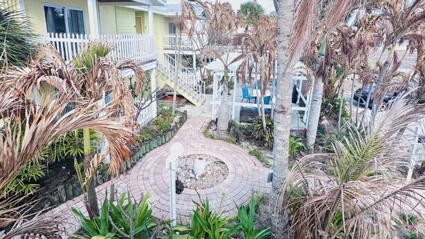 A residential area with a pathway leading to a house with a white fence and a small garden with palm trees and plants.