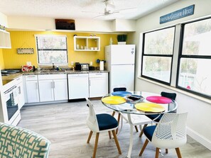 A kitchen with white cabinets, a refrigerator, and a dining area with a glass table and colorful chairs.