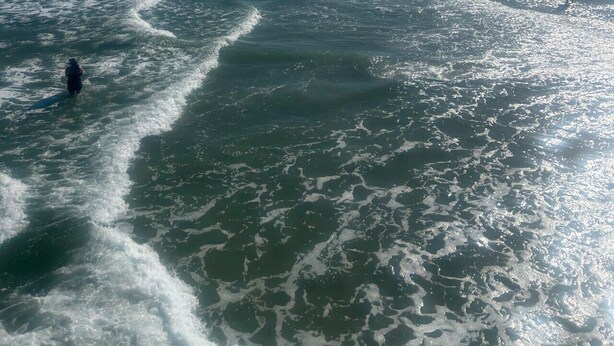 Ein Strand mit Wellen, Menschen und Gebäuden im Hintergrund.